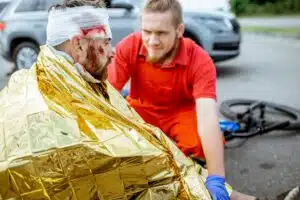 A paramedic caring for an injured cyclist wrapped in a thermal blanket with a head injury