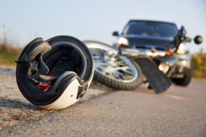 A motorycle helmet and motorcycle laying on the road in front of a car.