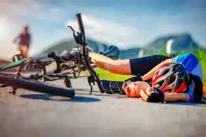 An injured cyclist lying unconcious next to their bike with a bloody knee
