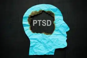 A blue paper cut out of a face on a black background with the words 'PTSD' in the brain area.
