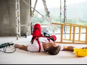 A worker lying unconscious on the ground next to a toppled over ladder.