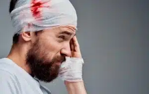 A man with a severe head injury. There is a bandage with blood wrapped around his head.