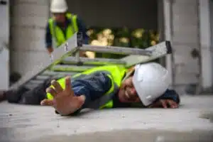 A construction worker laying on the ground reaching out for help with a ladder on top of him.