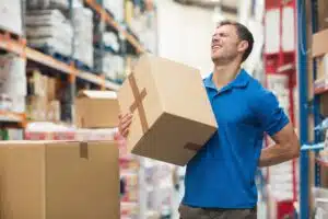 A warehouse worker carrying a box and holding his lower back in pain.
