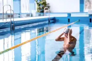 A man standing in a swimming pool adjusting his swim cap.